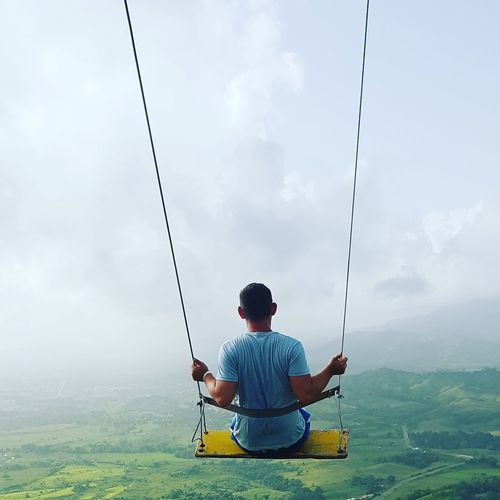 Rear view of man sitting on swing against sky