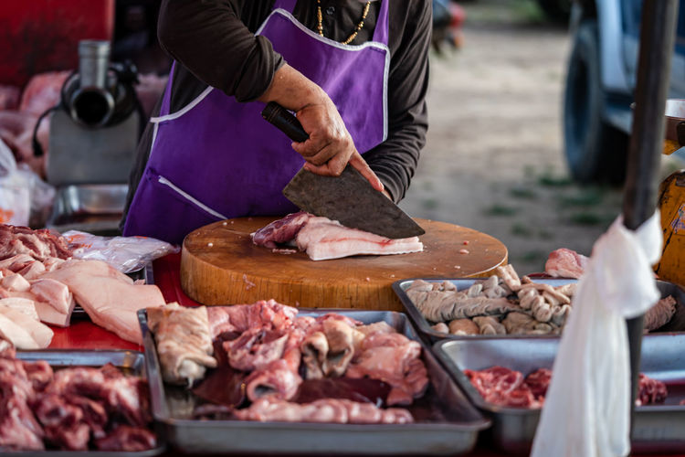 Image of a meat merchant use a knife to cut pork on a wooden cutting board to sell at rural markets.