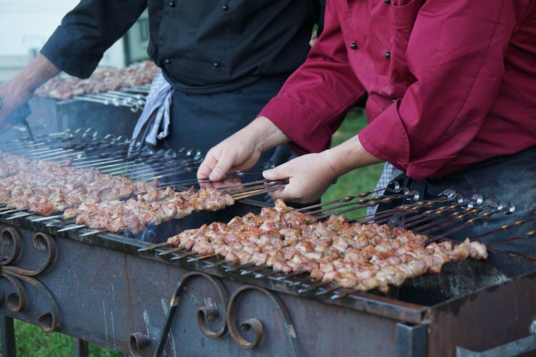 Midsection of men arranging kebab skewers on barbecue grill