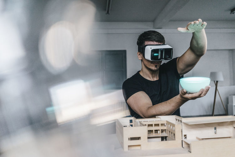 Man with architectural model and vr glasses holding bowl