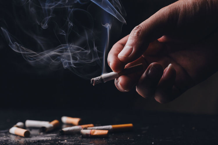 Cropped hand of person holding cigarette against black background
