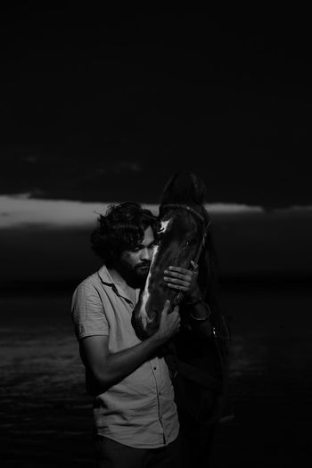 Young man embracing with horse on beach at night