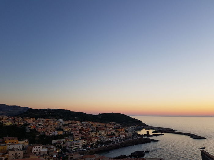 Townscape by sea against clear sky during sunset