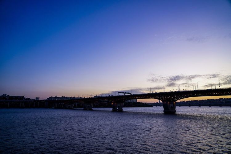 Bridge over river against blue sky during sunset