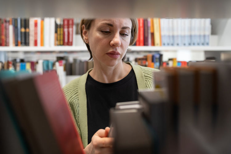Scandinavian middle-aged woman choosing textbook, looking for literature while preparing for exam