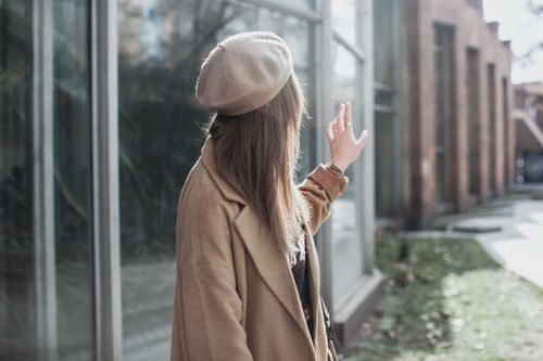 Side view of young woman waving by building