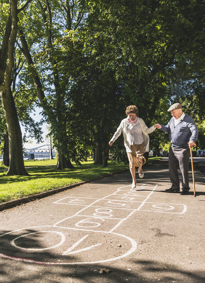 Senior woman playing hopscotch while husbanf watching her
