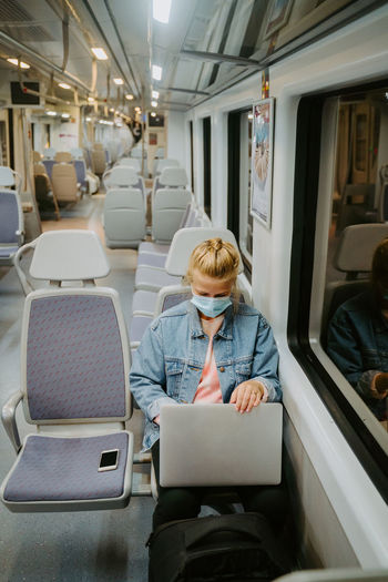 Concentrated female freelancer in medical mask browsing laptop while traveling by train