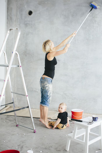 Young woman painting wall with son