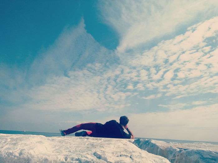 Rear view full length of man relaxing on rock against sky