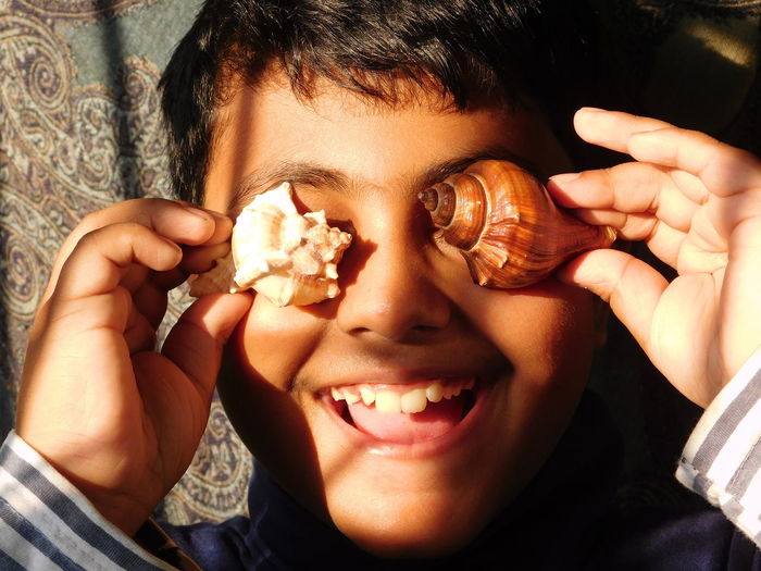 Close-up of cute boy holding seashells against eyes