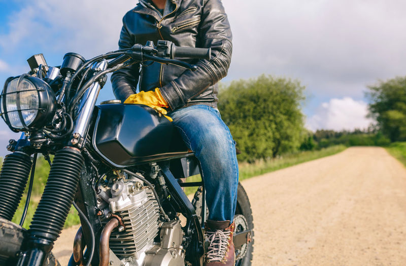 Low section of man sitting on motorcycle over road against sky