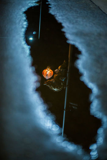 Reflection of statue with illuminated lantern on puddle at night