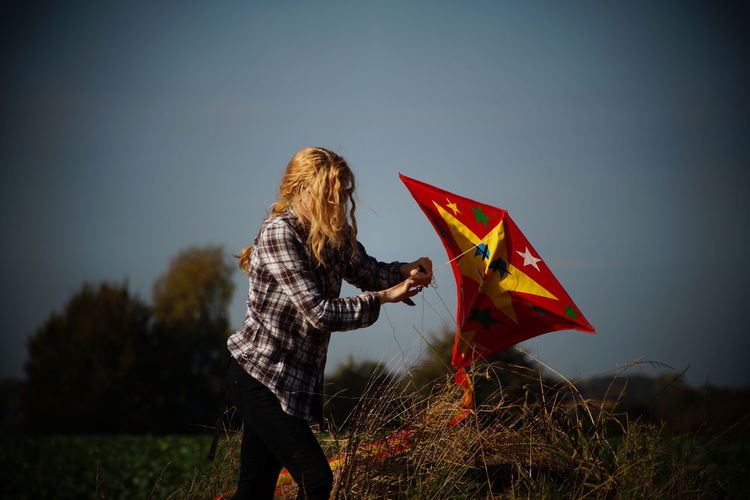 Woman holding kite while standing on field