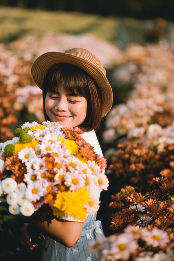 Woman wearing hat standing by flowering plants on field