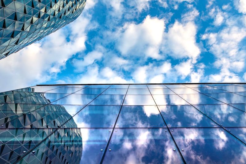 Low angle view of glass building against cloudy sky