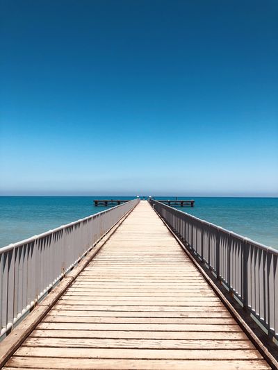 View of wooden jetty leading to sea against clear blue sky