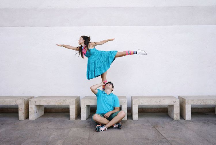 Man sitting by woman dancing against wall