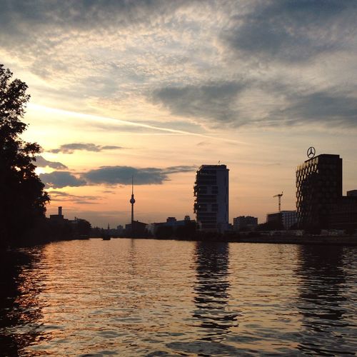 City skyline by river against sky during sunset