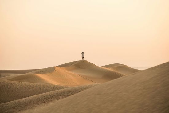 Distant view of woman standing on sand dune at desert against clear sky