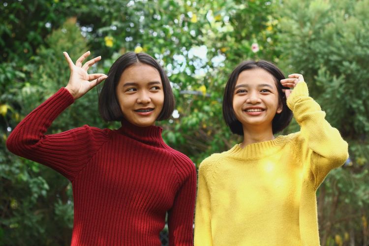 Smiling teenage friends looking away while standing against plants