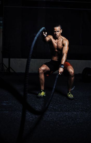 Portrait of muscular man exercising battle rope in gym
