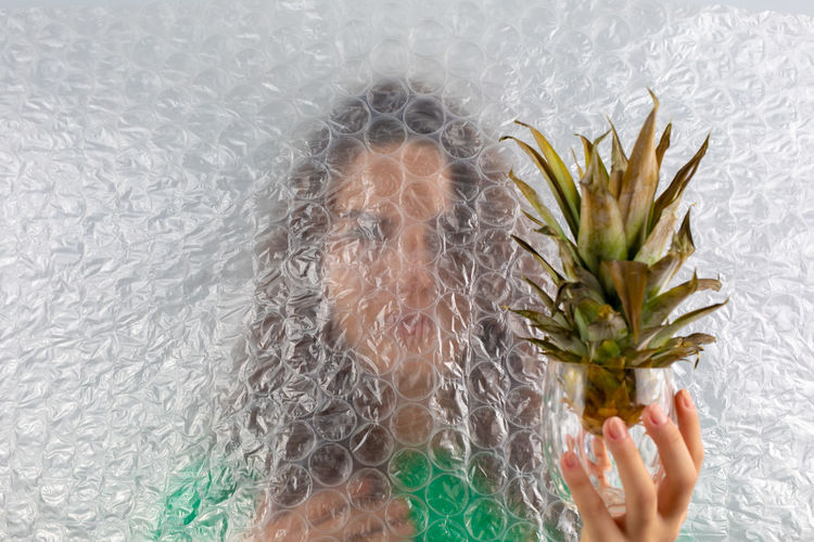 Close-up of woman hand holding pineapple in glass seen through bubble wrap over face