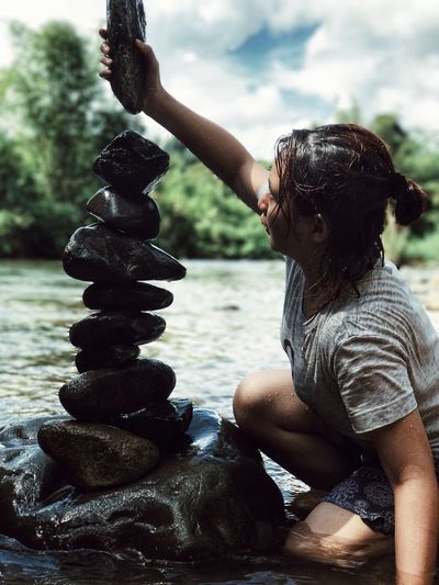 Young woman stacking pebbles by river