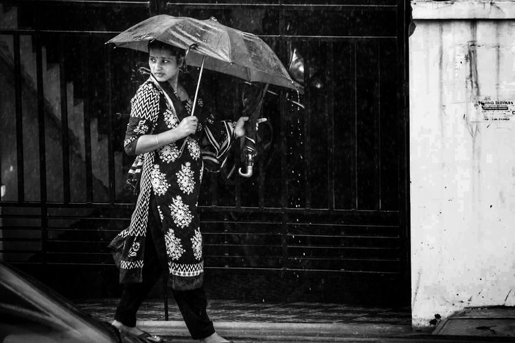 Full length of woman walking with umbrellas by gate in rain