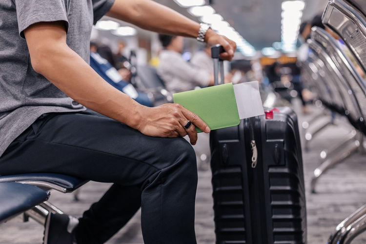 Midsection of man with luggage sitting at airport