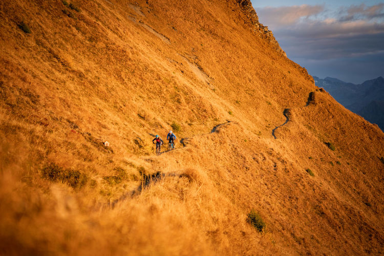 Men cycling on mountain road against sky