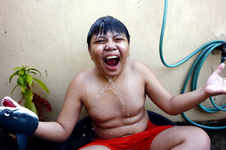 Asian boy cooling down in a water basin and a hose as a makeshift shower to beat the summer heat.