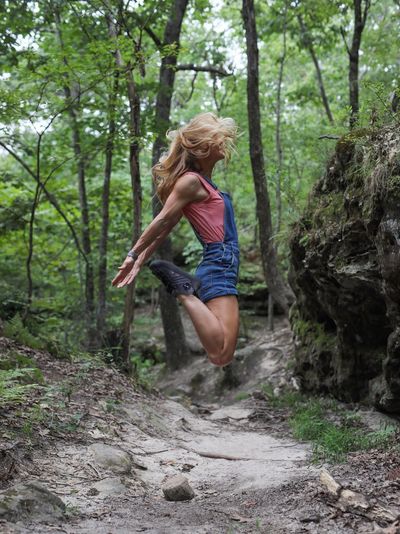 Full length of young woman jumping in forest