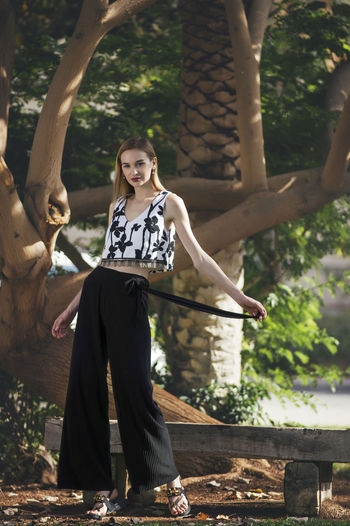 Portrait of young woman standing against trees in park