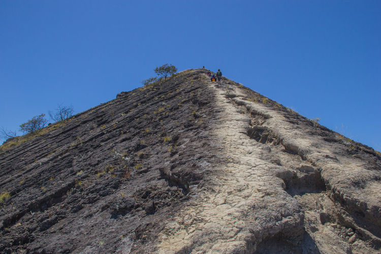 Low angle view of people on mountain against clear blue sky