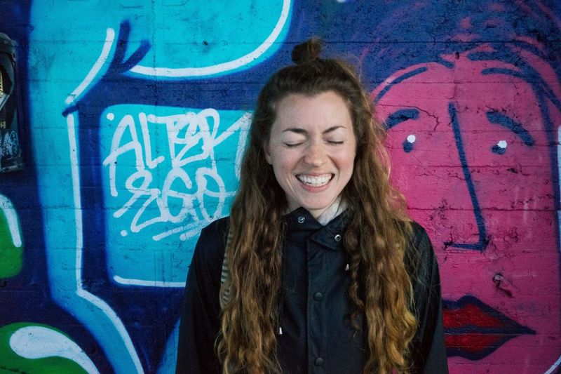 Young woman laughing against graffiti on wall