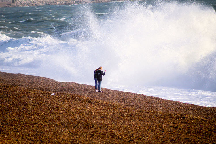 Rear view of man standing on sea shore against sky