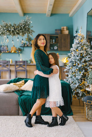 Beautiful mom and daughter in stylish clothes hug in the christmas living room