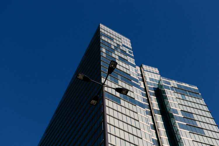 Low angle view of modern building and street light against clear blue sky