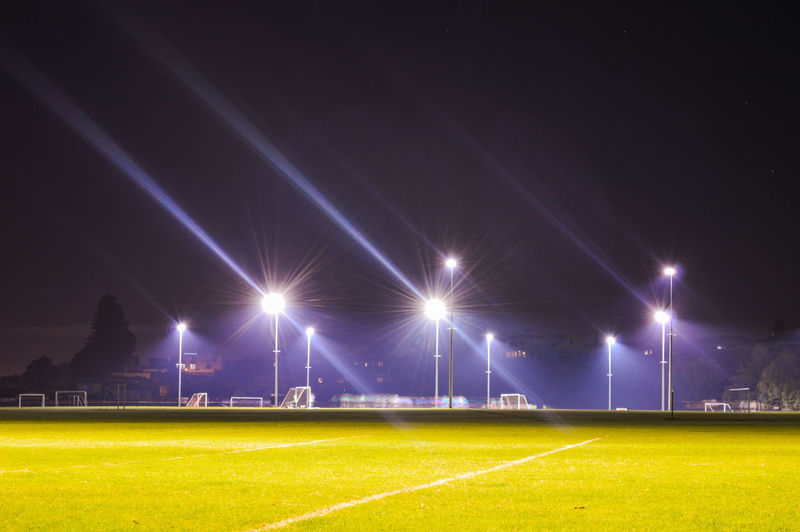 Illuminated lights on field against sky at night