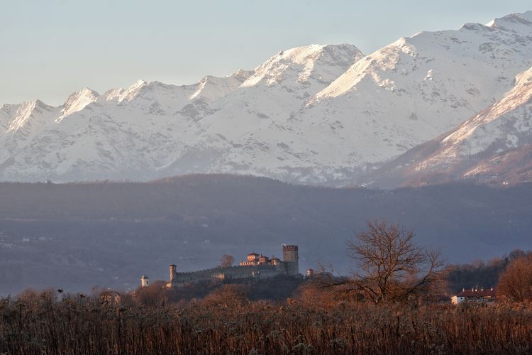Some mountains of piedmont, italy, covered with snow, with an ancient castle nearby 