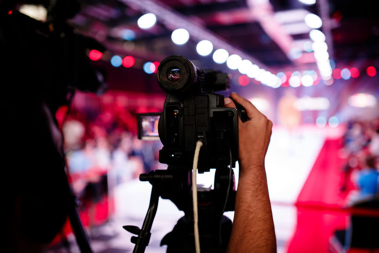 Cropped hand of photographer adjusting television camera on tripod at fashion show