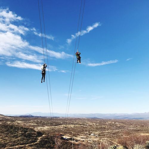 Low angle view of people zip lining over mountain against sky