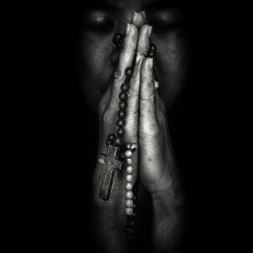 Close-up of woman praying with rosary in darkroom