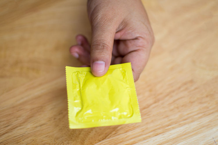 Close-up of man holding condom on table