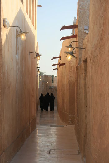 Rear view of people walking on narrow street amidst buildings