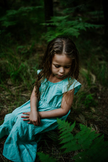Vertical portrait of young girl looking down surrounded by ferns