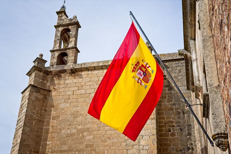 Flag of spain in front of an old church in cáceres