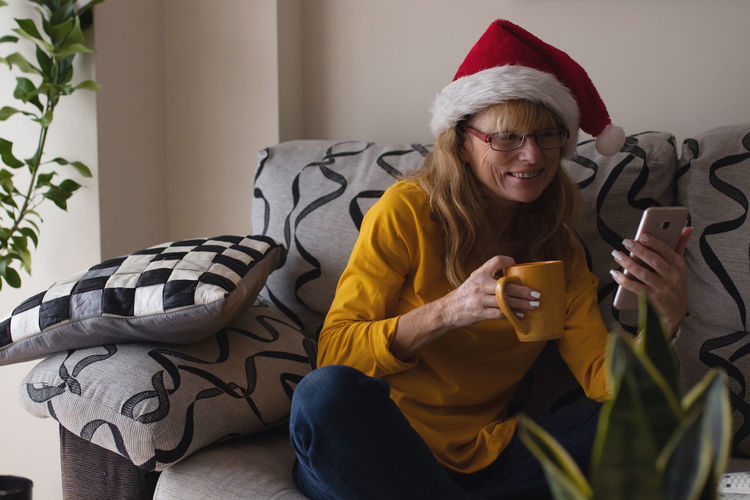 Portrait of young woman using mobile phone while sitting on sofa at home