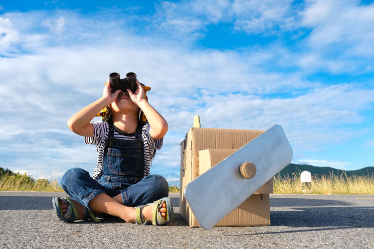 Side view of woman photographing with binoculars while standing against sky